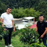 Nestor Lasso and sibling standing next to a sidra coffee plant at their farm, Finca El Diviso. Processing facilities are located in the background.