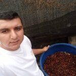 Nestor Lasso stands next to a container filled with bourbon sidra coffee cherries.